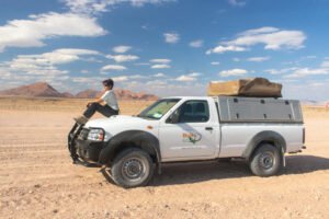 Roberta Martins no capô de um carro com barraca em cima viajando pelo deserto da Namíbia